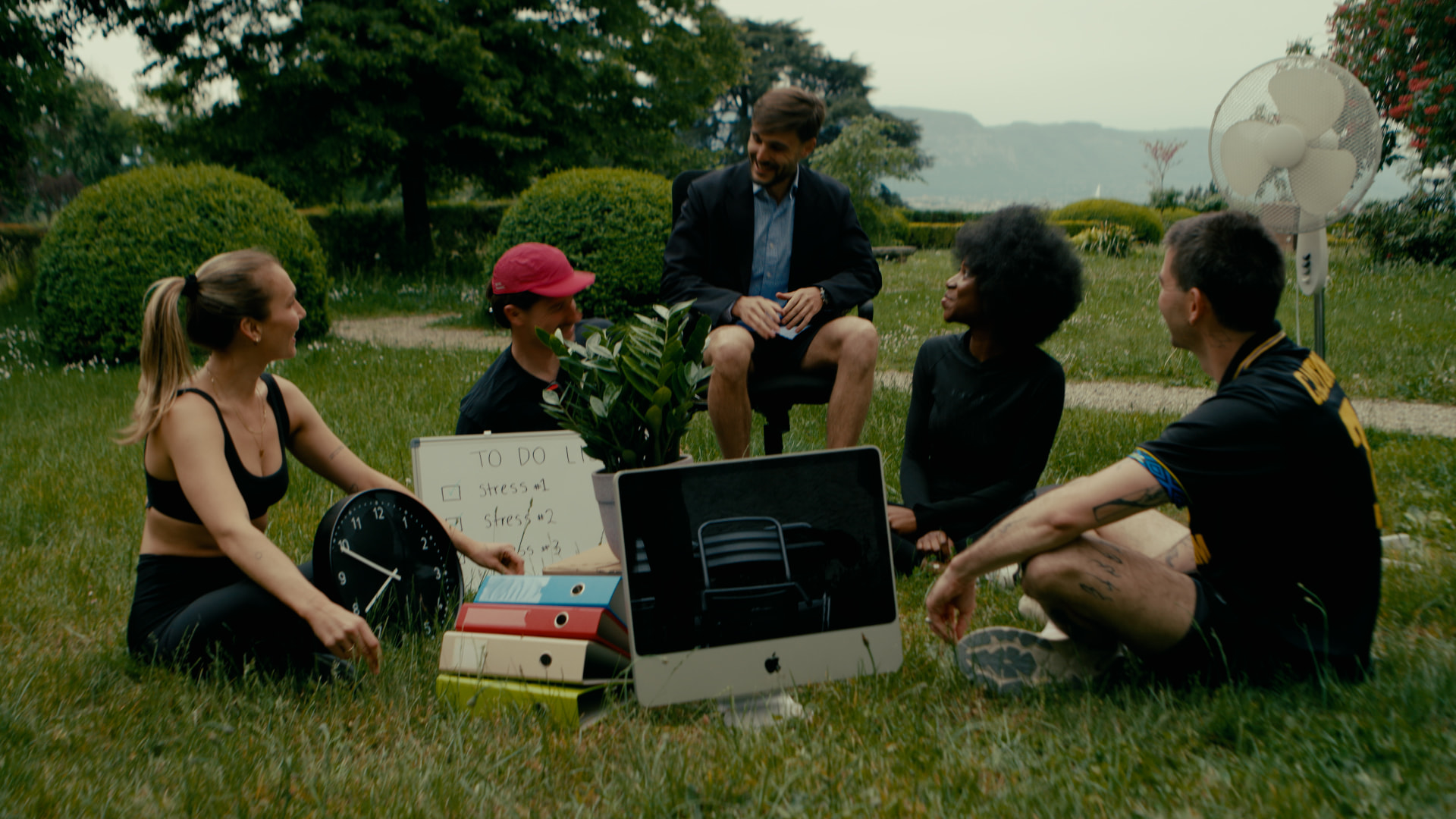 A team sitting in a circle on the grass with office props around them